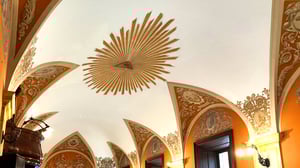 Dettaglio della volta affrescata della sala conferenze dell’Ospedale dell’Isola Tiberina a Roma, con al centro il simbolo dell’occhio radiante e decorazioni barocche in ocra e oro