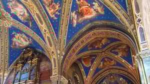Dettaglio del soffitto affrescato della Basilica di Santa Maria sopra Minerva a Roma, con volte decorate, figure celestiali e organo a canne dorato.
